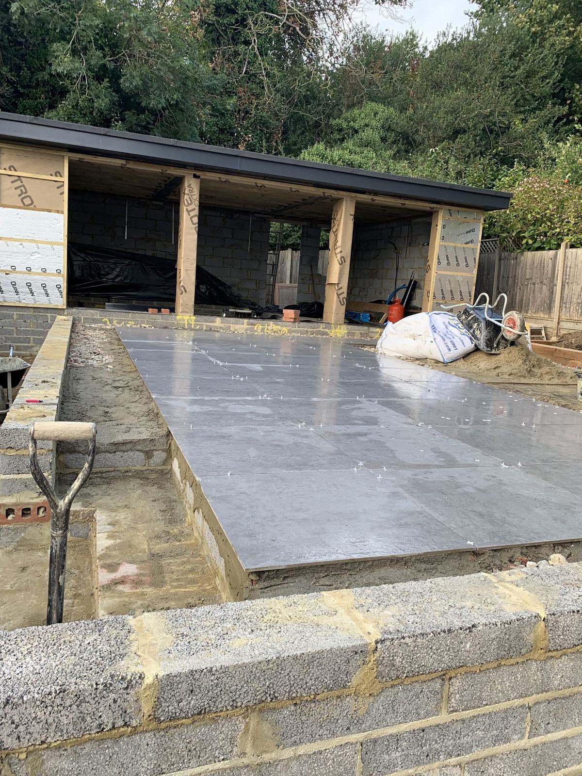 Large-format porcelain going down on a prepared, free-draining base in front of the new garden building.