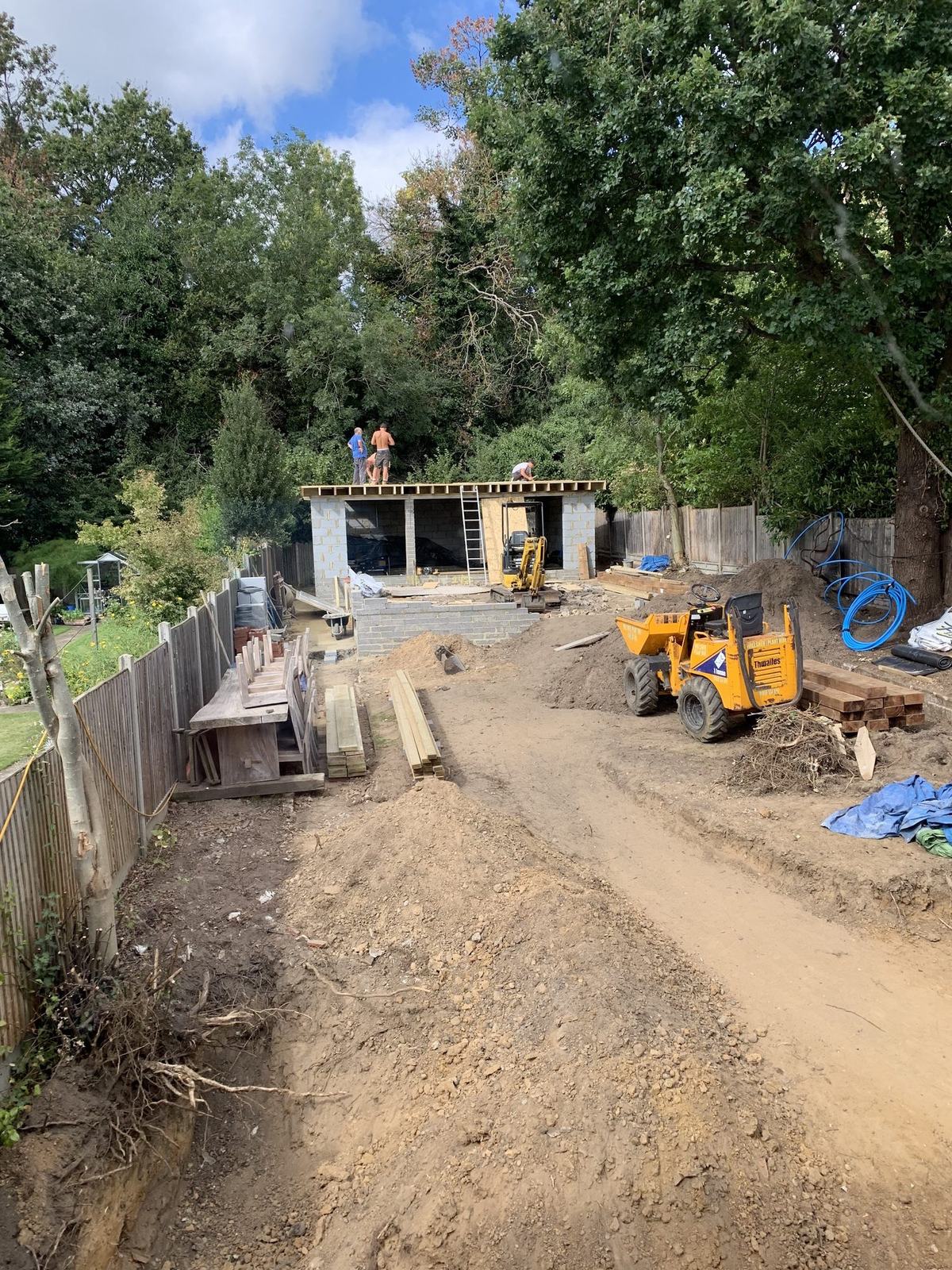 Mid-project: the plot cleared and levelled, the garden room’s frame and flat roof up, and access kept open for the dumper.